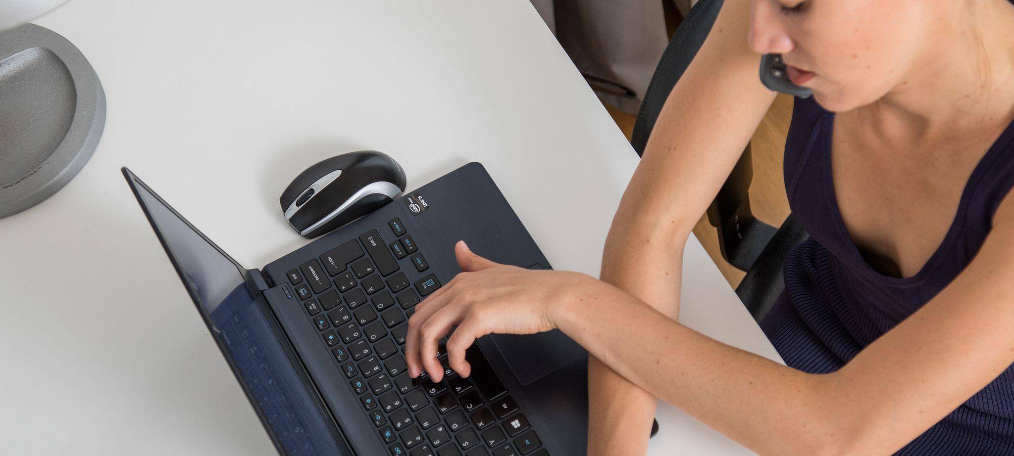 Eine Frau telefoniert, tippt auf Laptop und schreibt Notiz