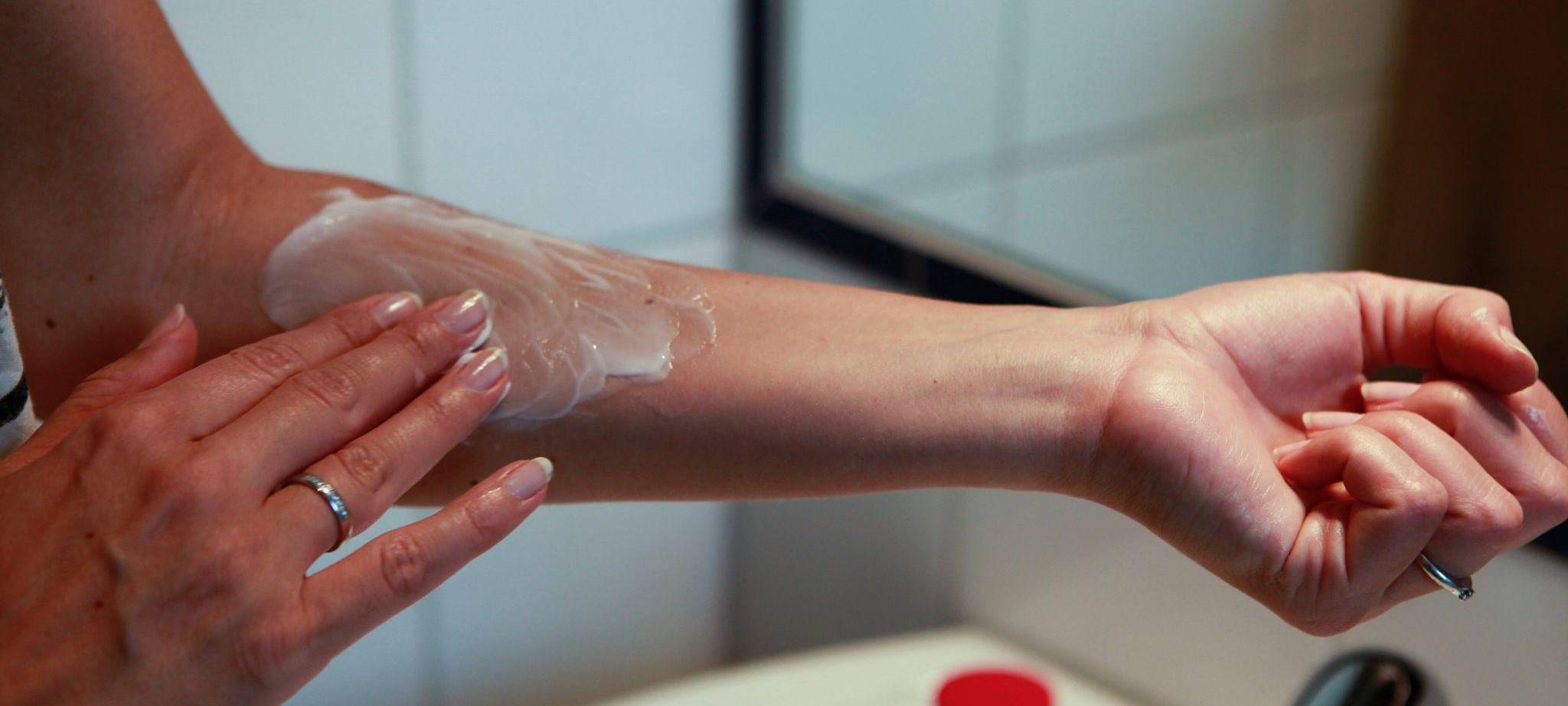 Frau cremt sich einen Arm ein