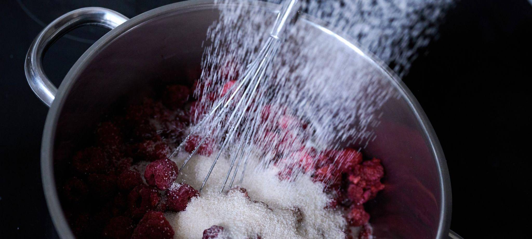Frau schüttet Gelierzucker auf Himbeeren, die eingekocht werden